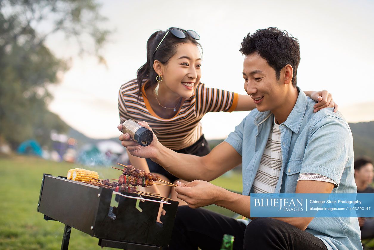 Happy young Chinese couple barbecuing outdoors