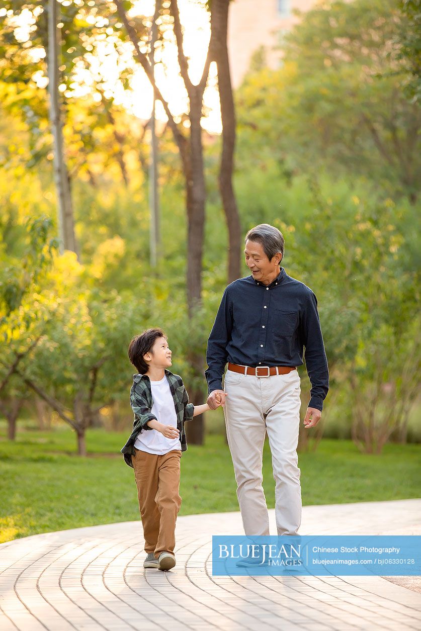 Happy Chinese grandfather and grandson walking in park