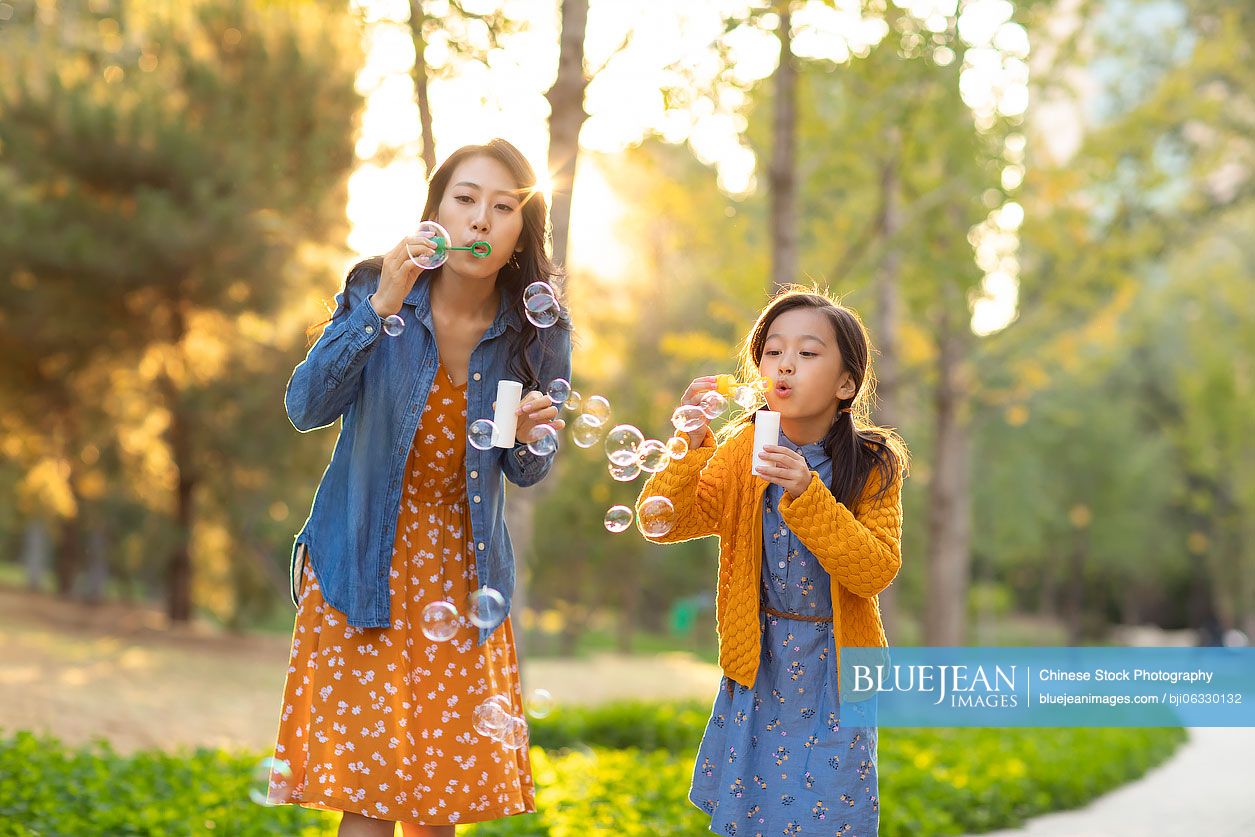 Happy Chinese mother and daughter blowing bubbles in park