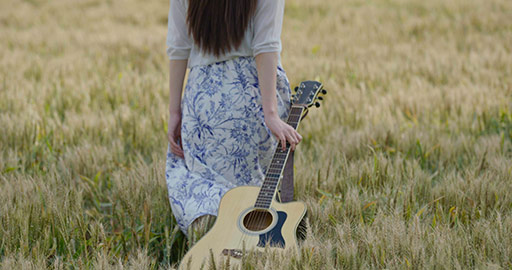 年轻女子拿着吉他在麦田里行走
