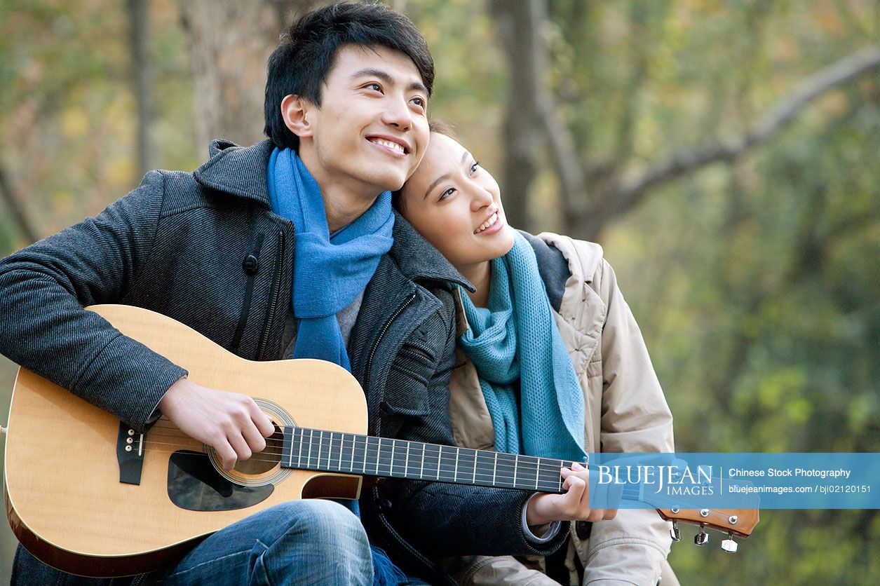 A young Chinese man plays the guitar as he girlfriend leans on him affectionately