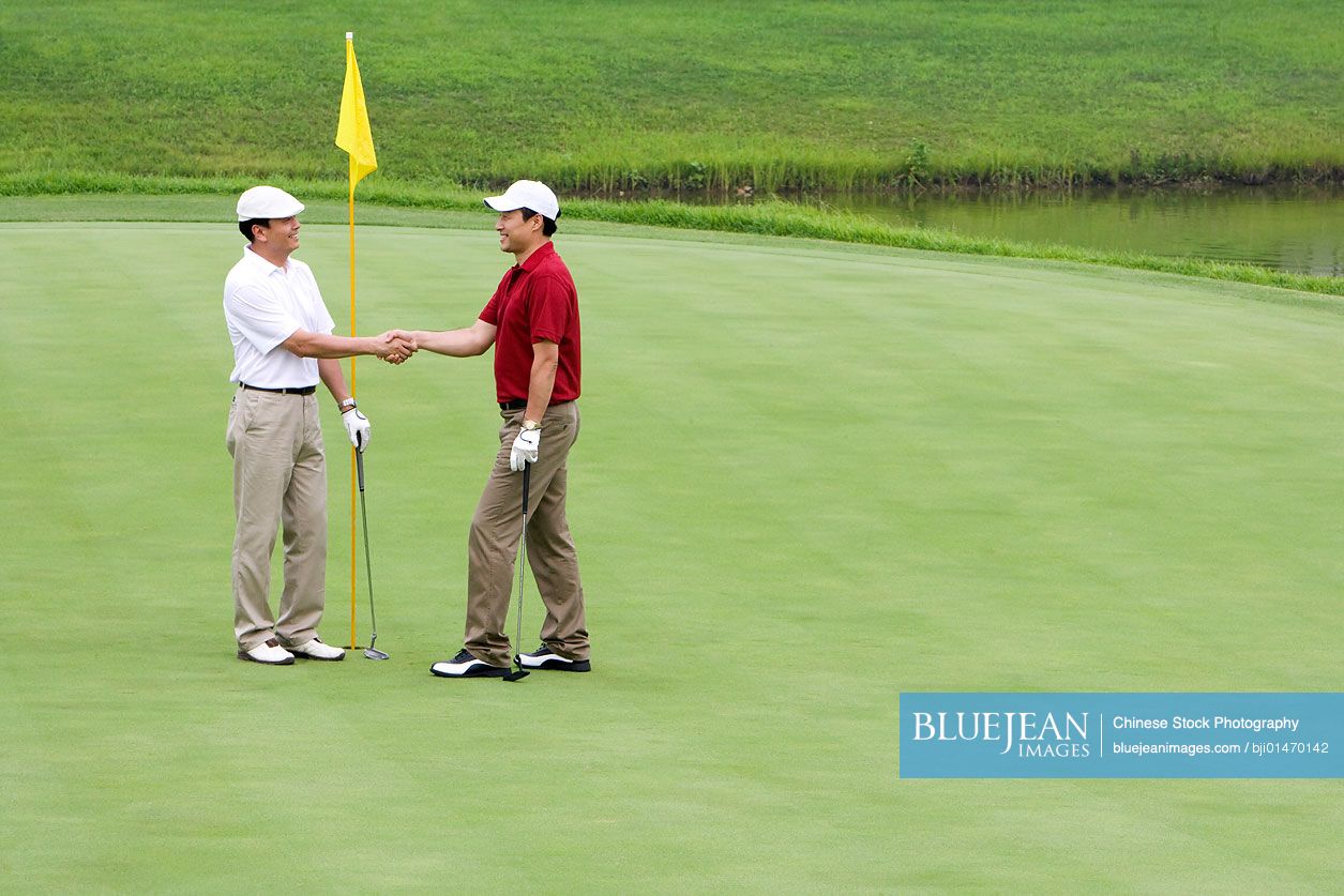 Two Chinese golfers shaking hands on the green
