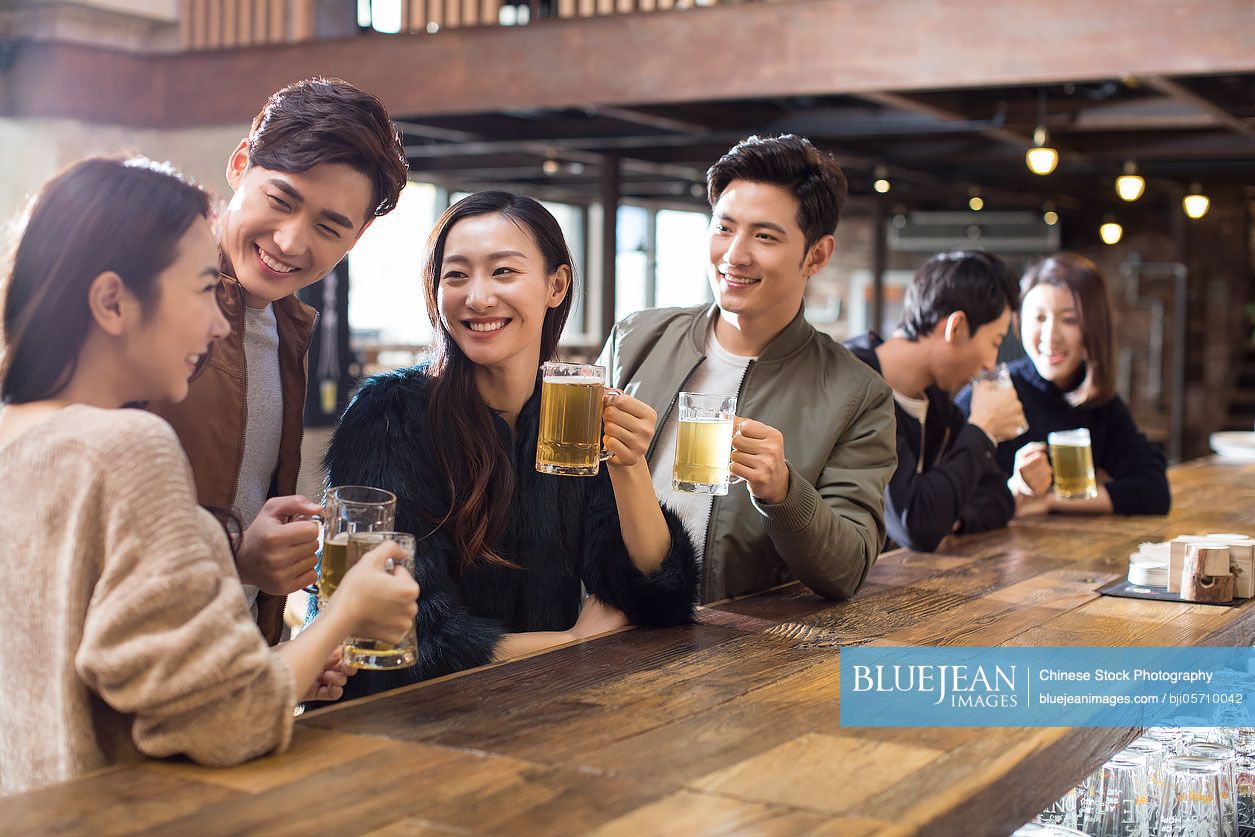 Happy Chinese friends drinking beer and talking in bar