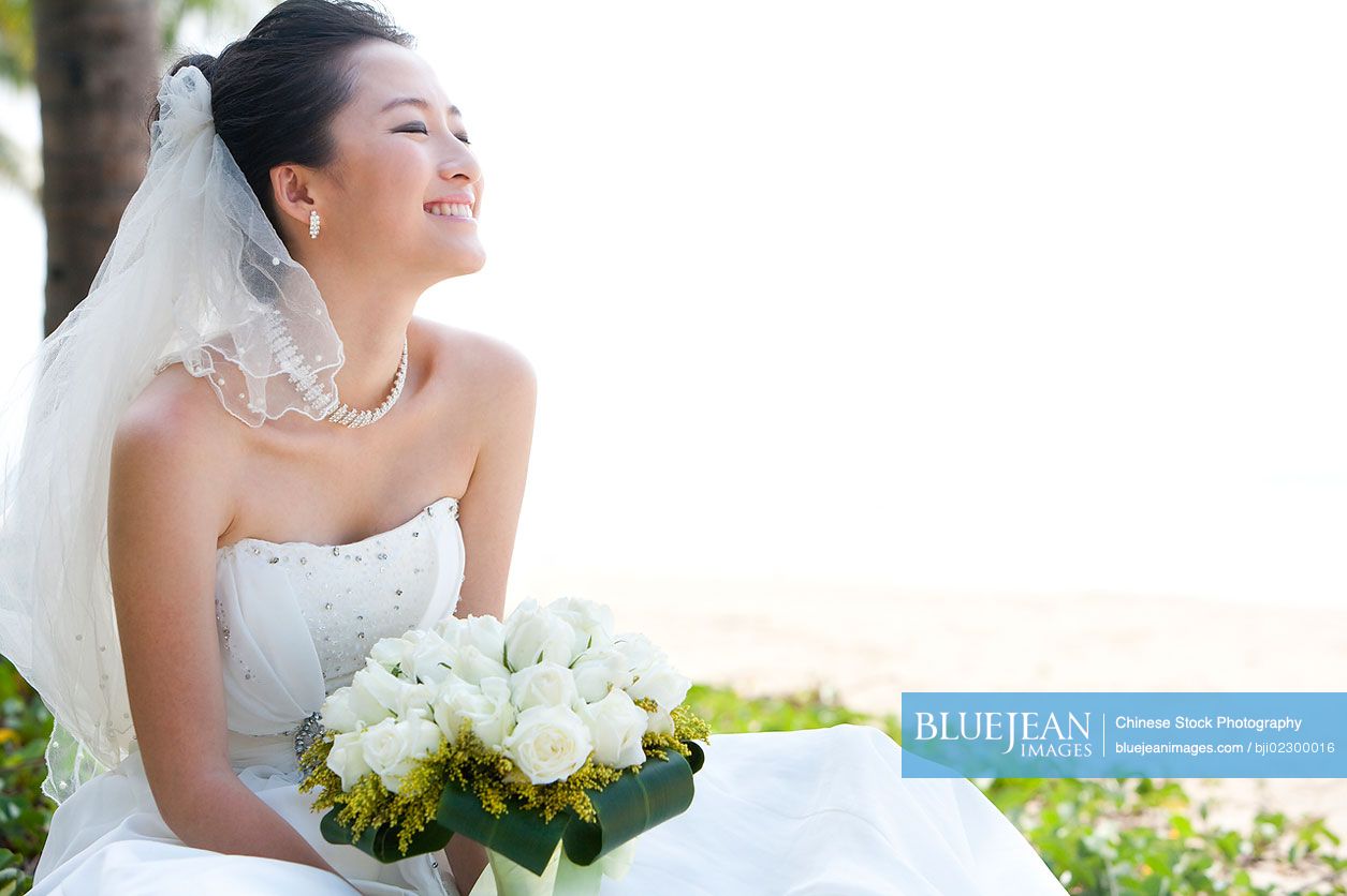 Happy Chinese bride sitting on the beach
