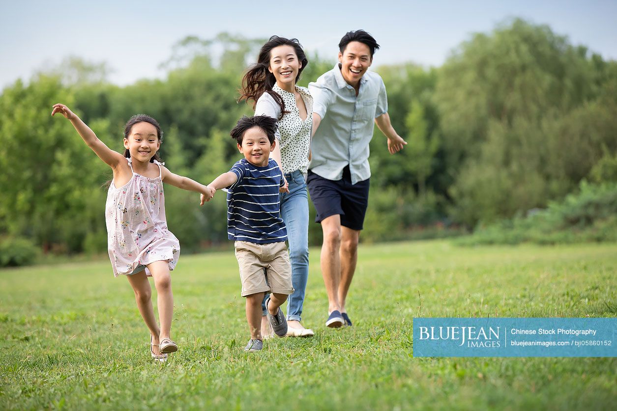 Happy young Chinese family running on grass