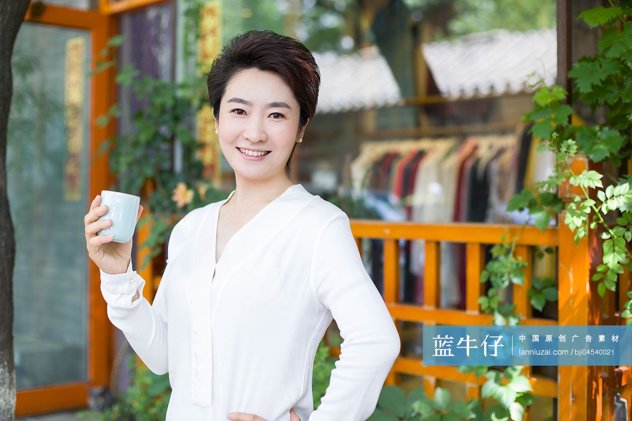 女性店主拿着茶杯站在店外