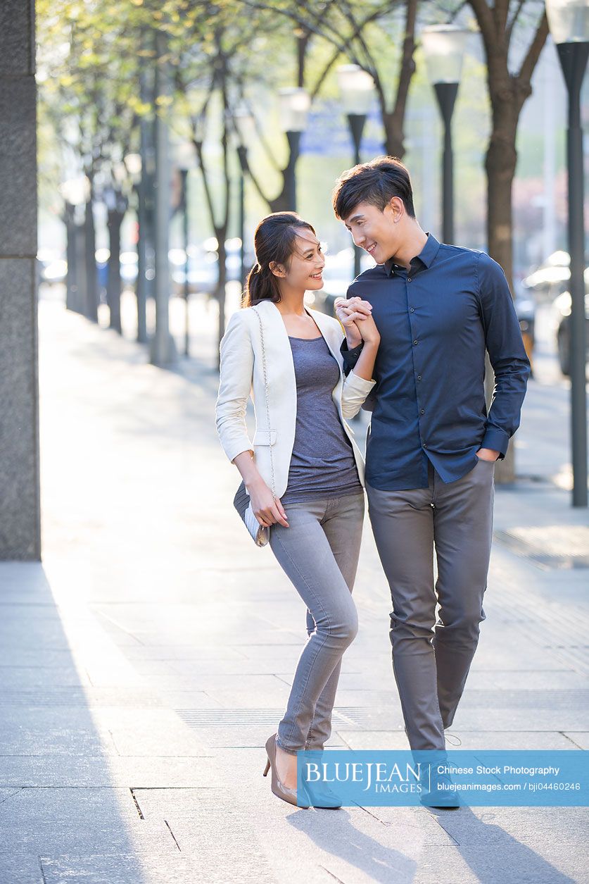 Young Chinese couple holding hands walking on sidewalk