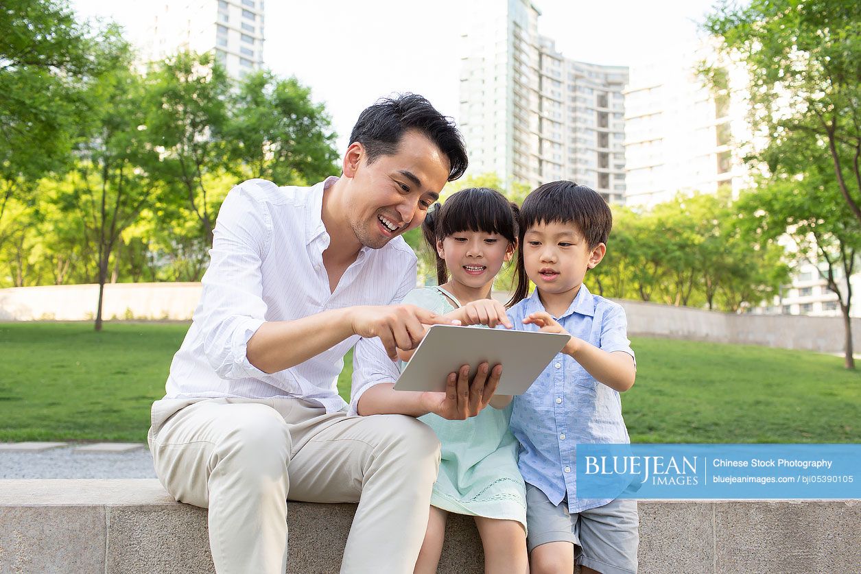 Happy young Chinese father and children using digital tablet