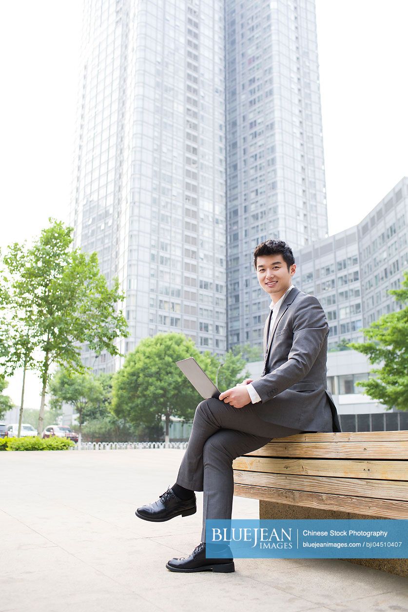 Young Chinese businessman working with laptop outdoors
