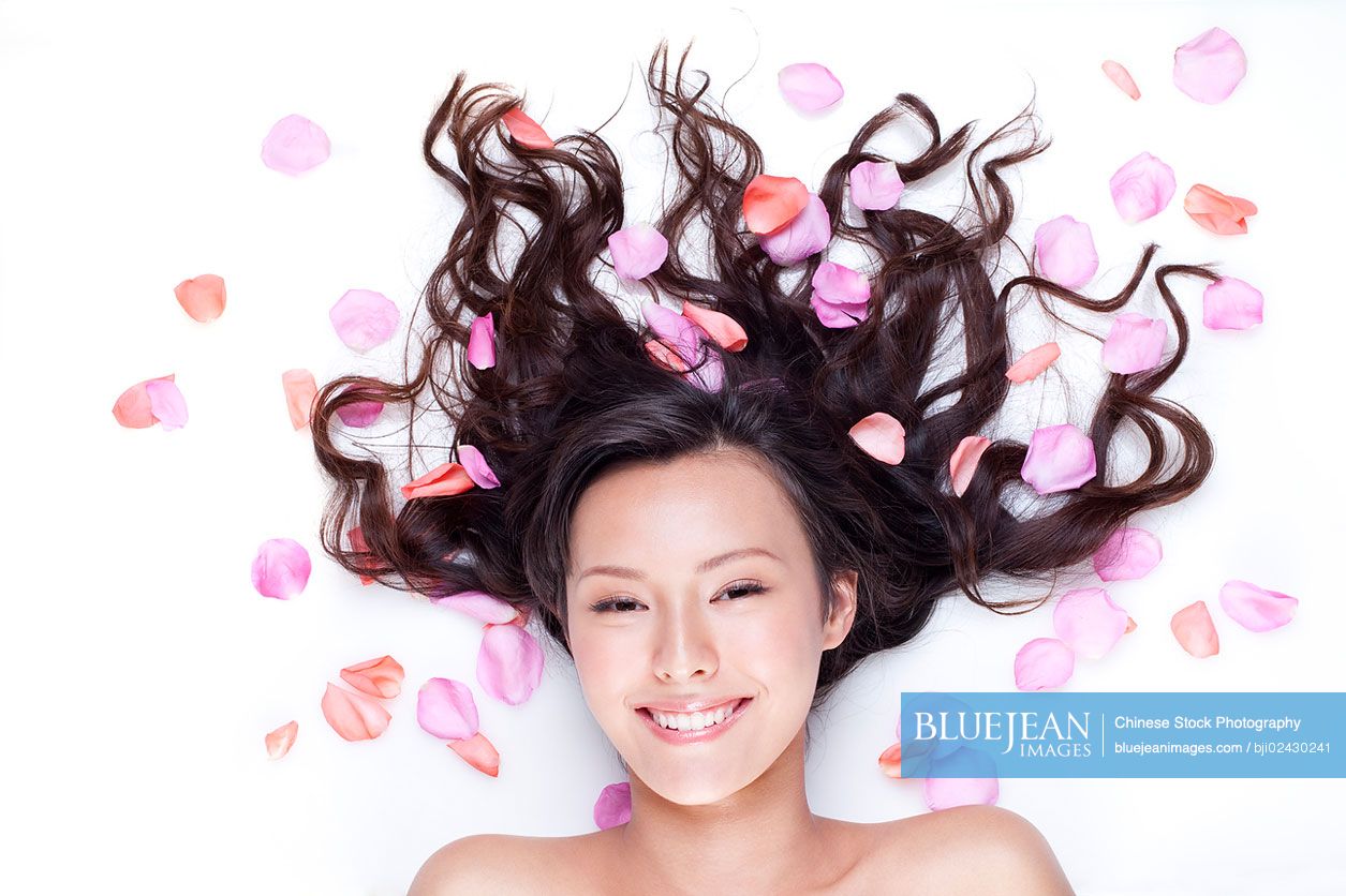 Portrait of beautiful young Chinese woman lying down surrounded by flowers