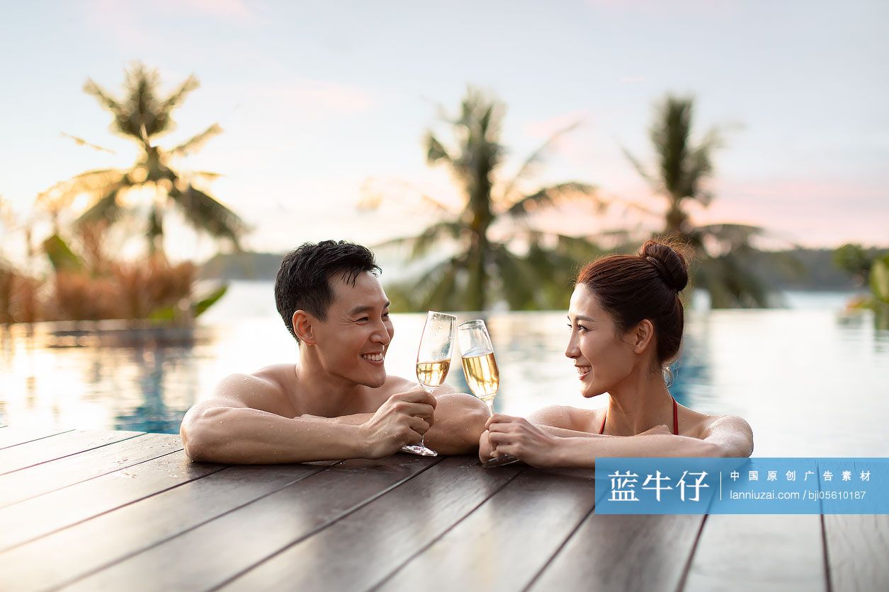 快乐的年轻情侣在泳池边喝香槟