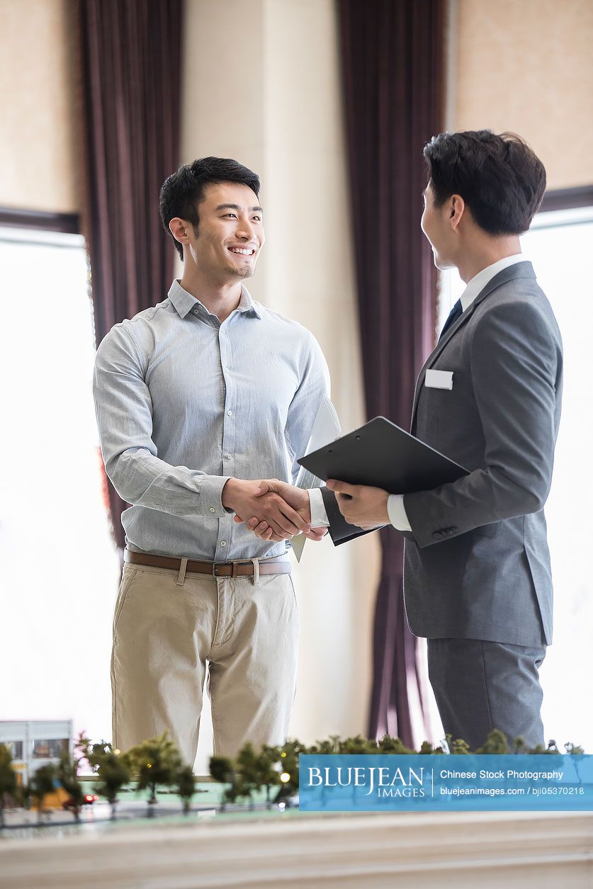 Happy young Chinese man shaking hands with realtor