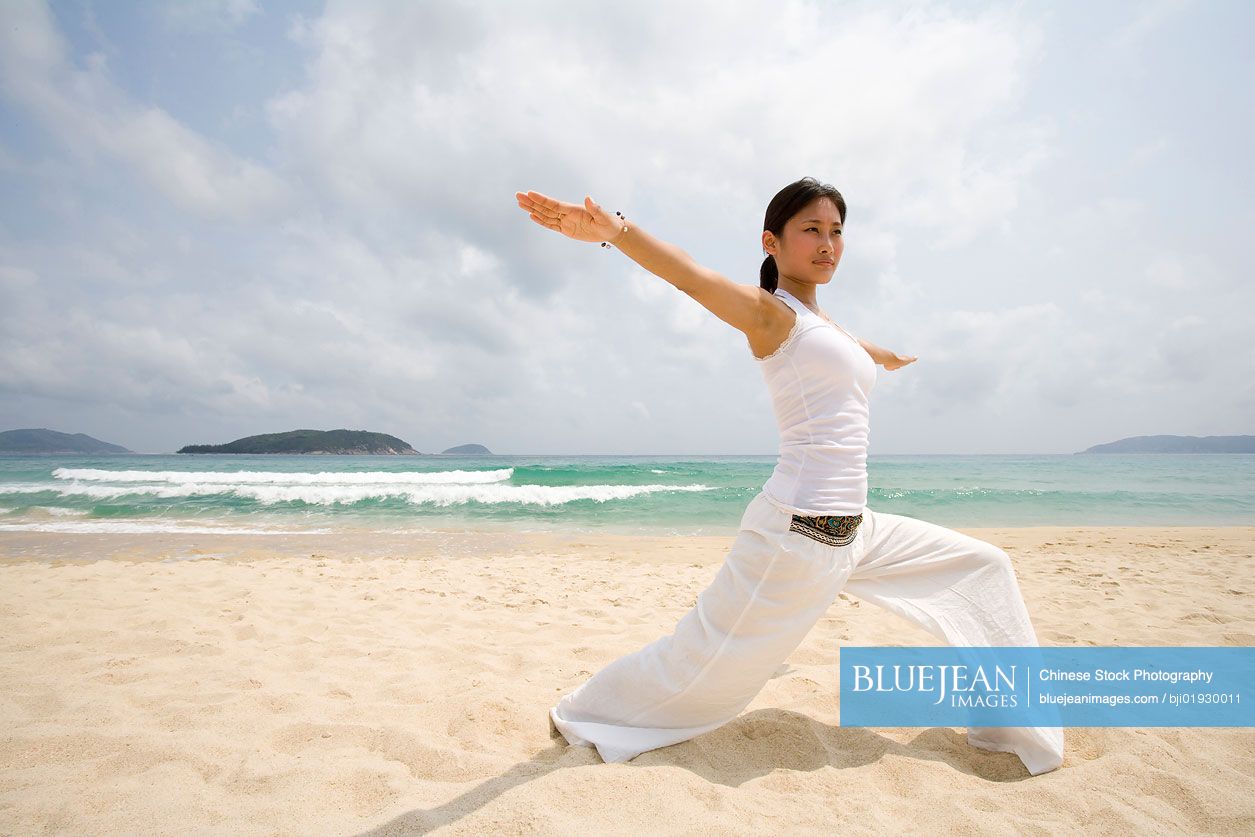 Young Chinese woman doing yoga on the beach