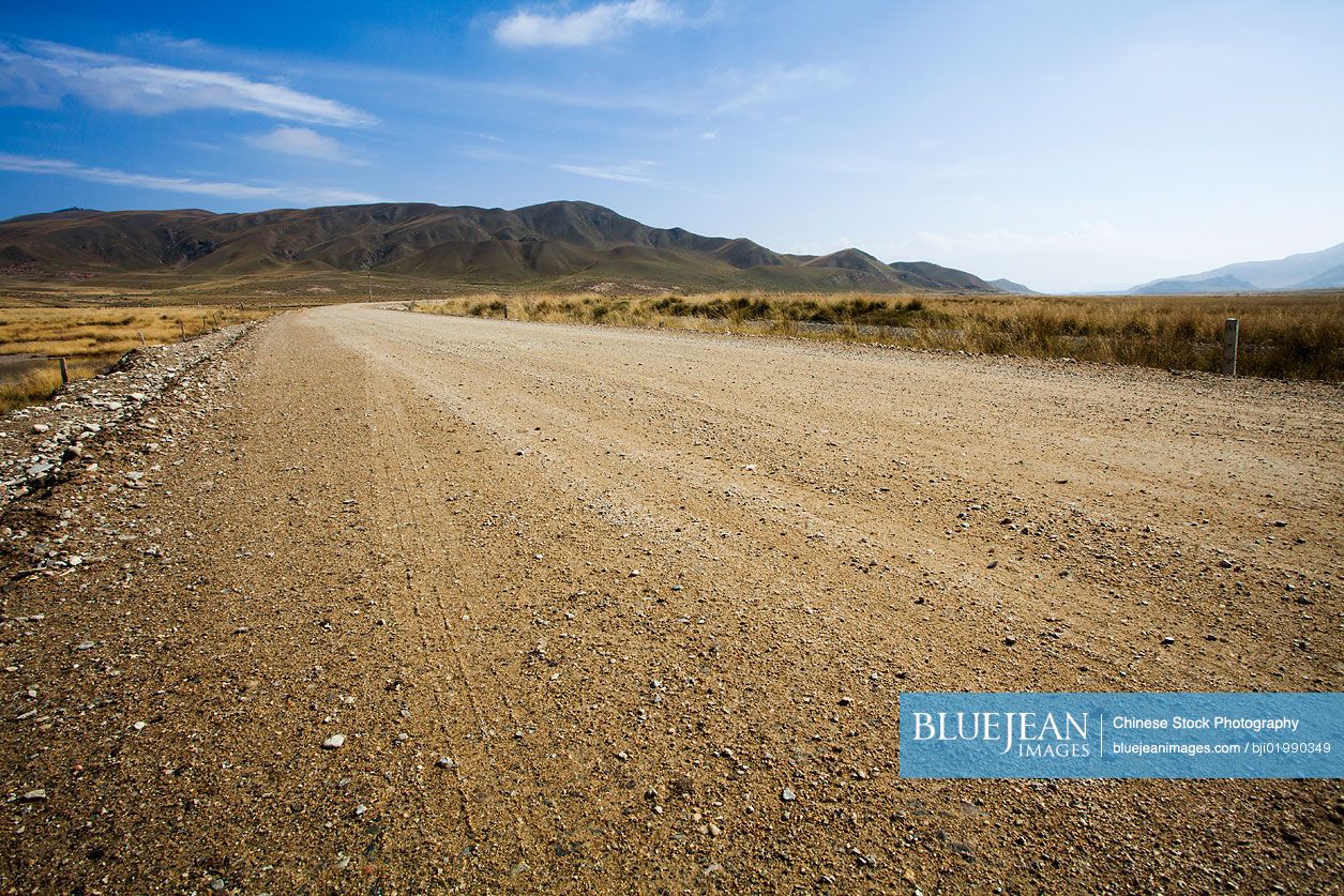 Gravel road going through field into the mountains in Qinghai province, China
