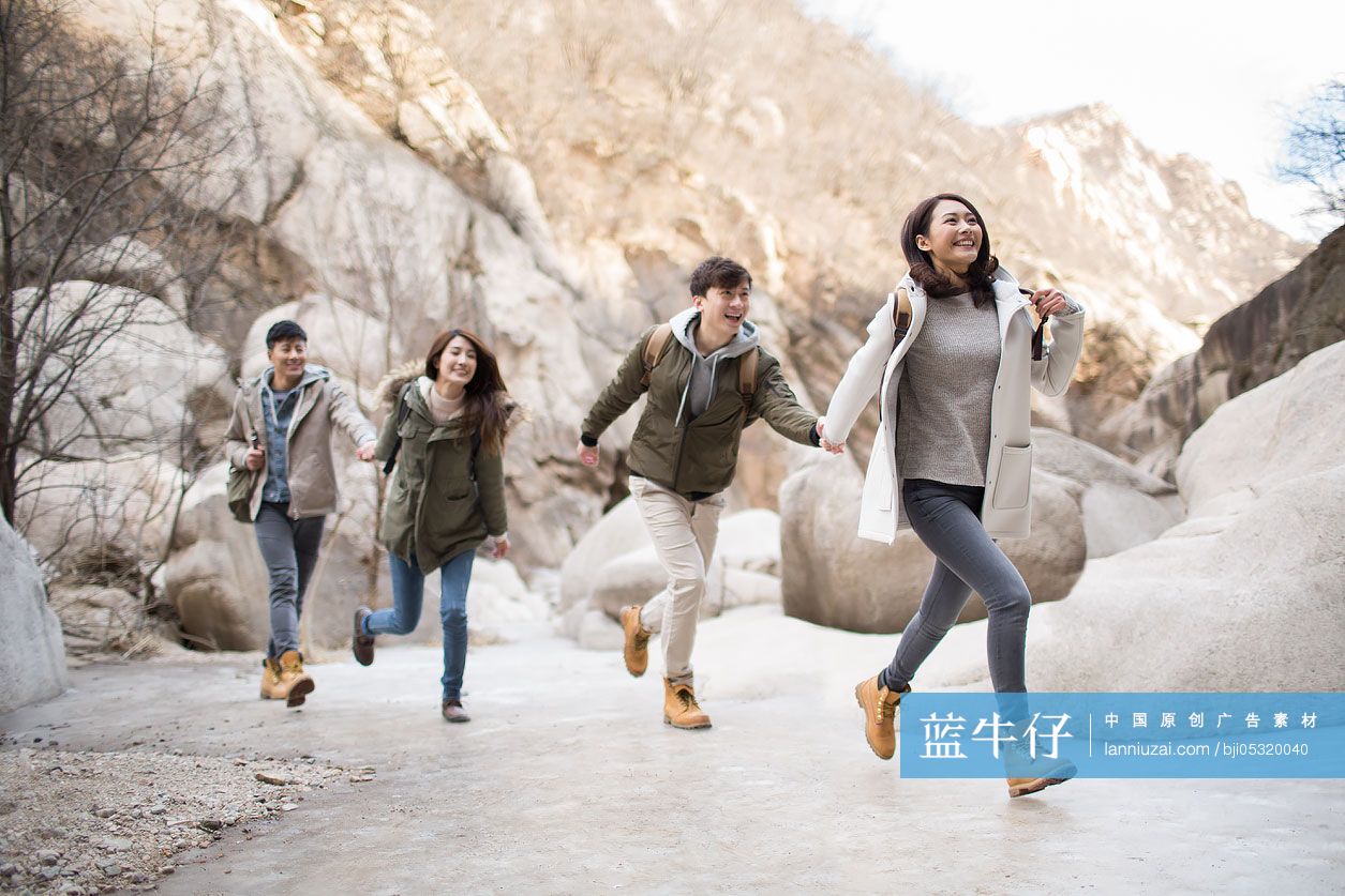 Happy young Chinese friends holding hands running outdoors in winter