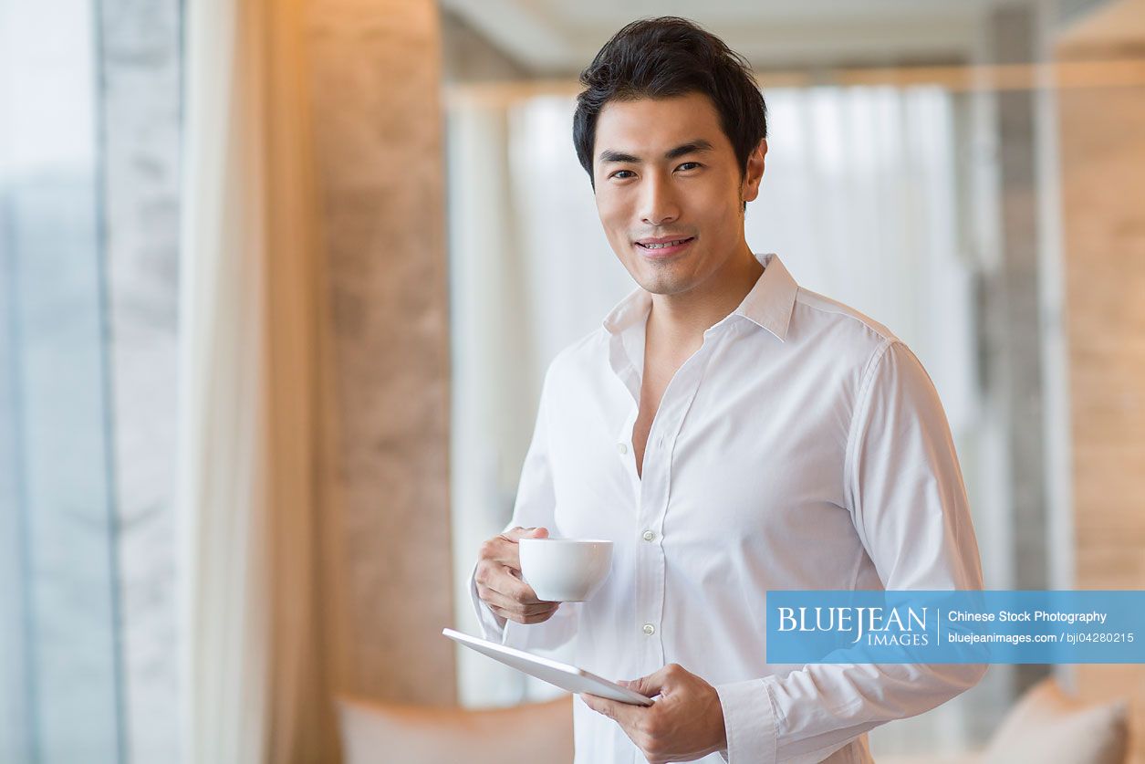 Young Chinese man drinking coffee with digital tablet