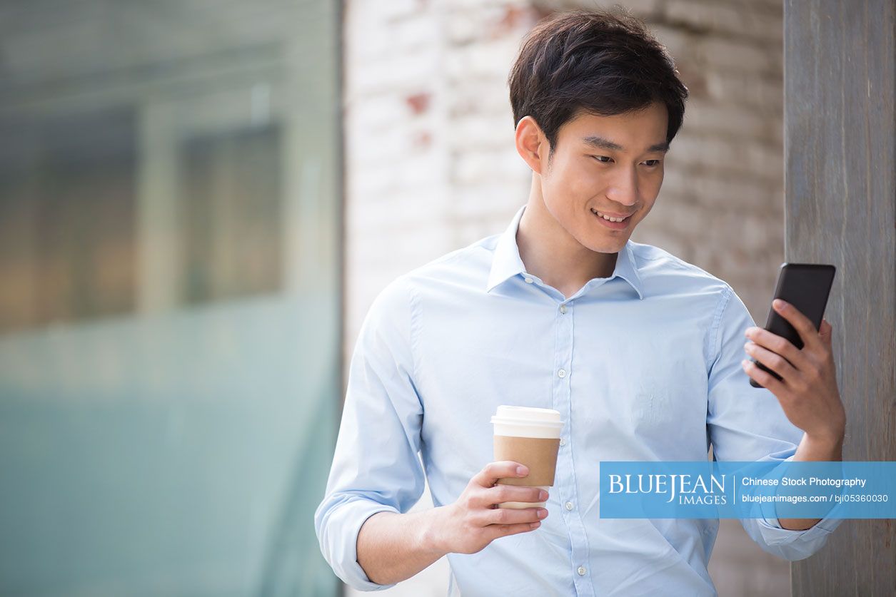 Young Chinese businessman with smart phone and coffee