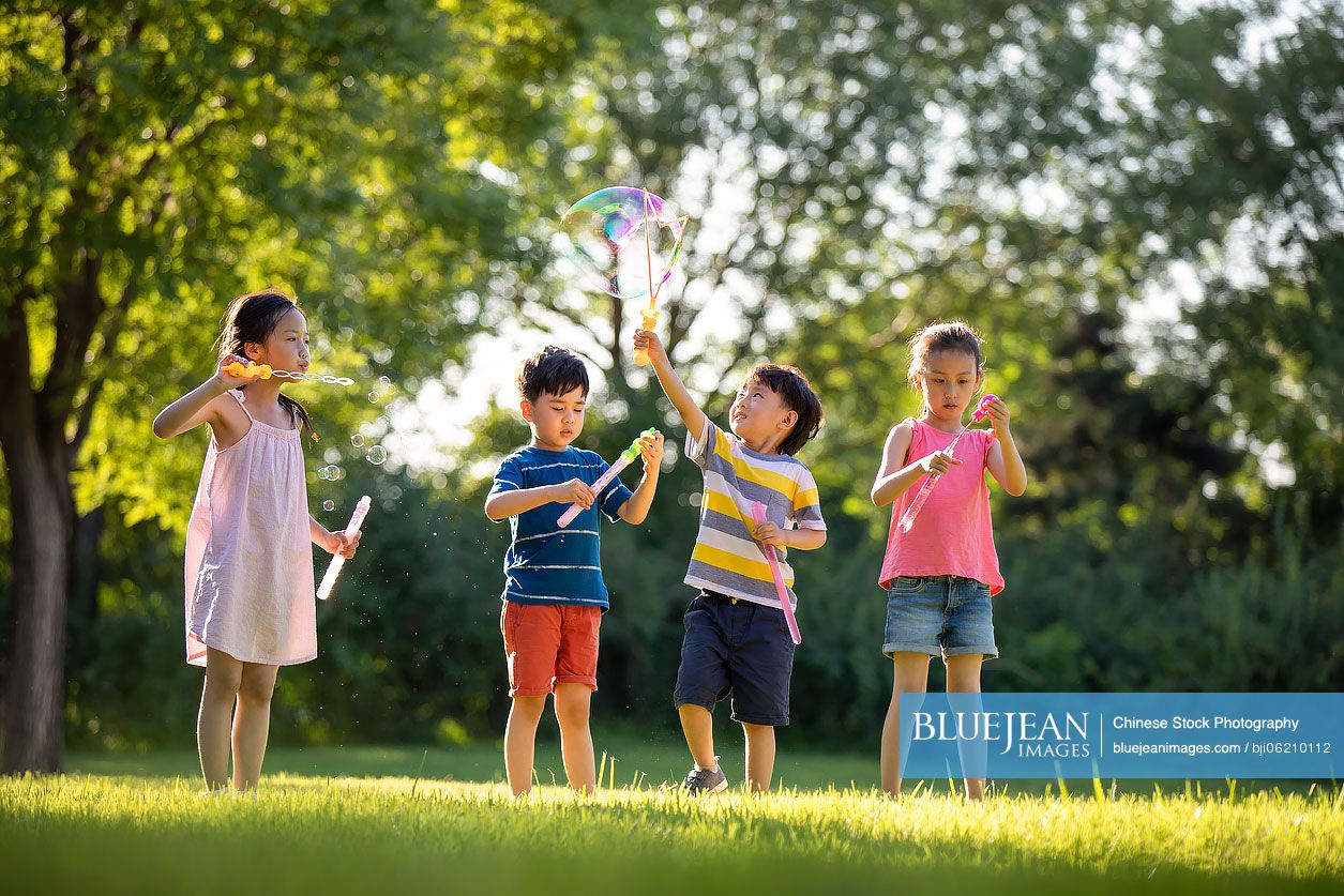 Happy Chinese children blowing bubbles on meadow