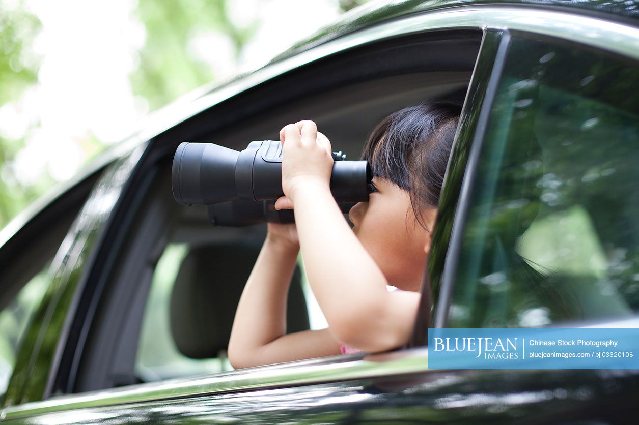 Cute Chinese girl looking through the car window with binoculars