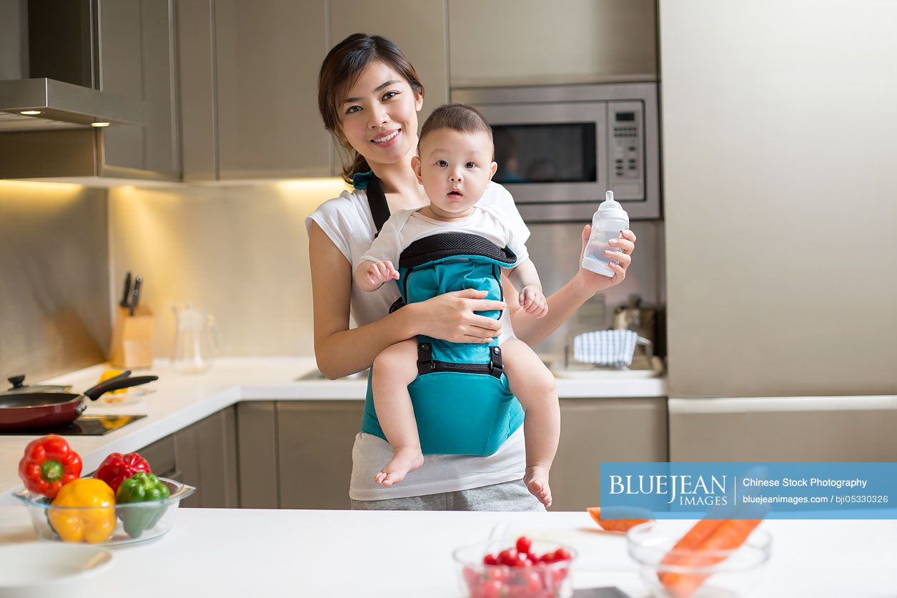 Chinese mother holding baby and cooking in the kitchen