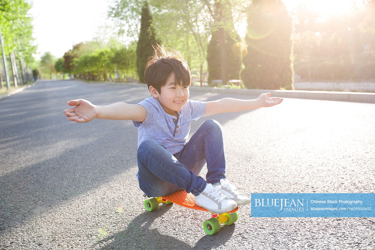 Little Chinese boy sitting on a skateboard