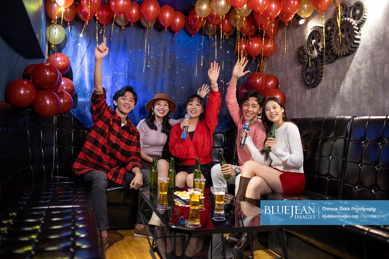 Happy young Chinese friends singing karaoke in nightclub