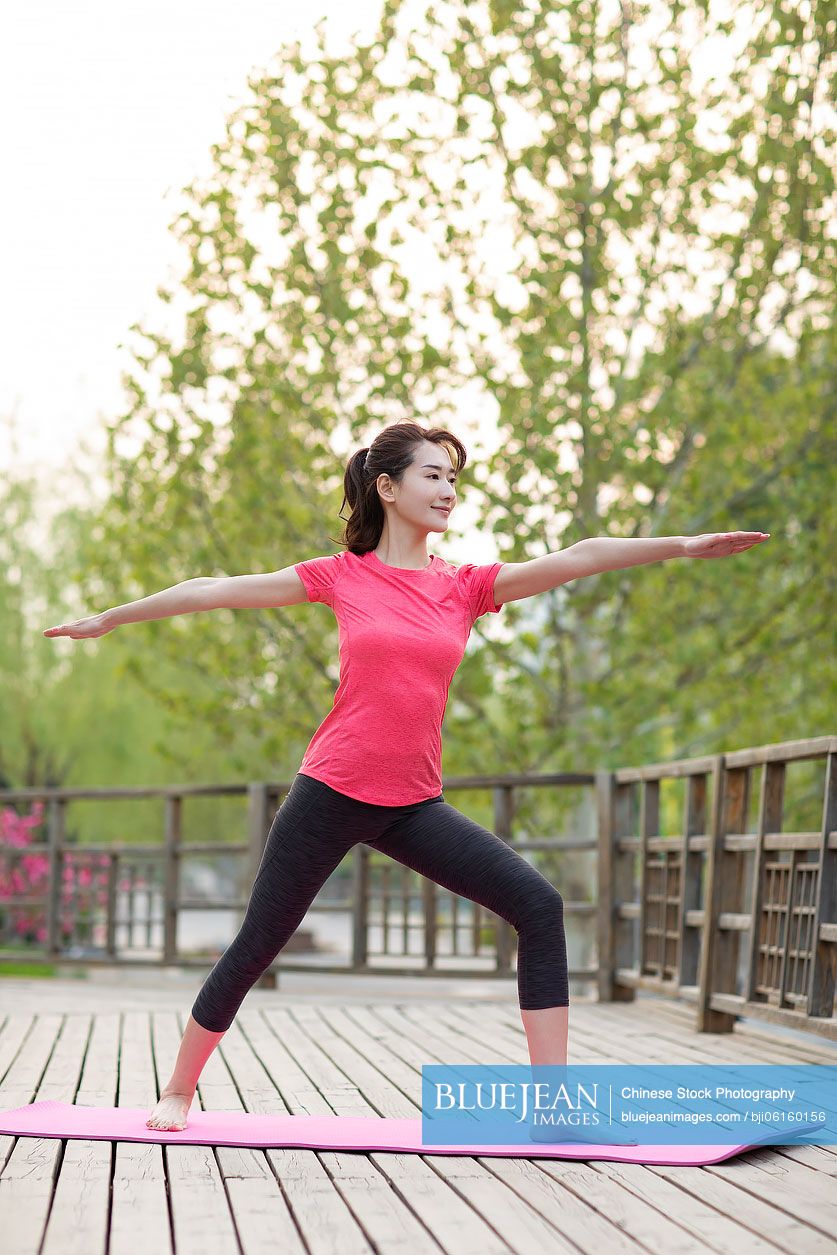 Happy young Chinese woman doing yoga in park