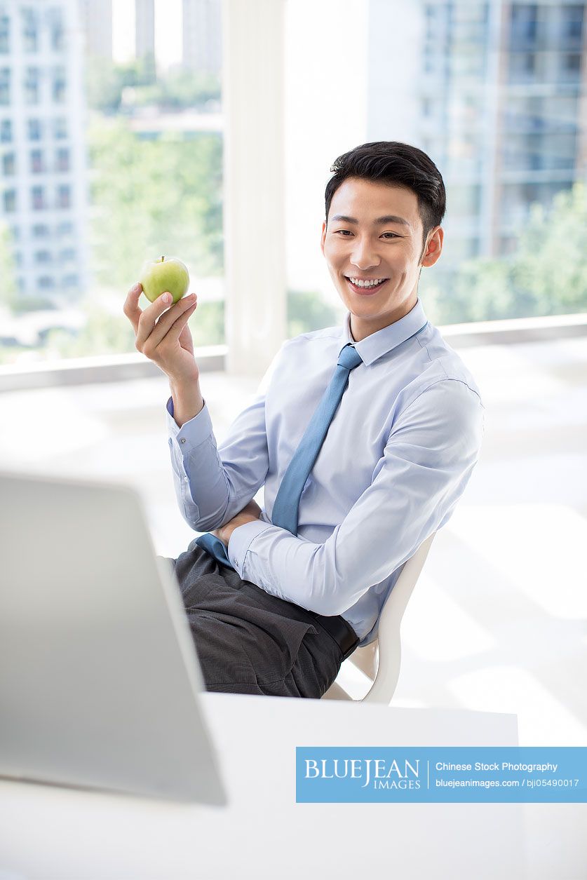 Young Chinese businessman holding an apple in office