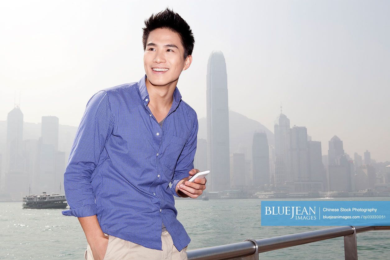 Happy young Chinese man enjoying himself in Victoria Harbor, Hong Kong