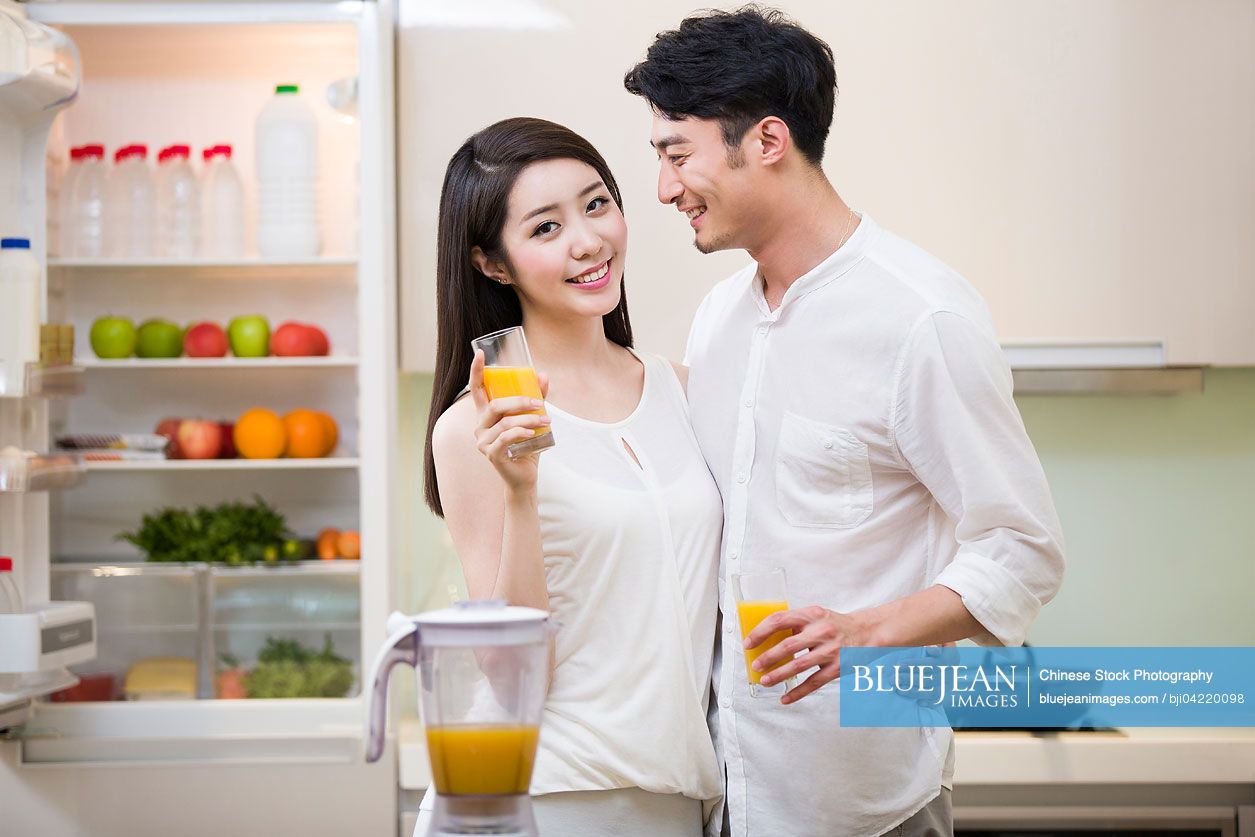 Young couple holding orange juice in kitchen