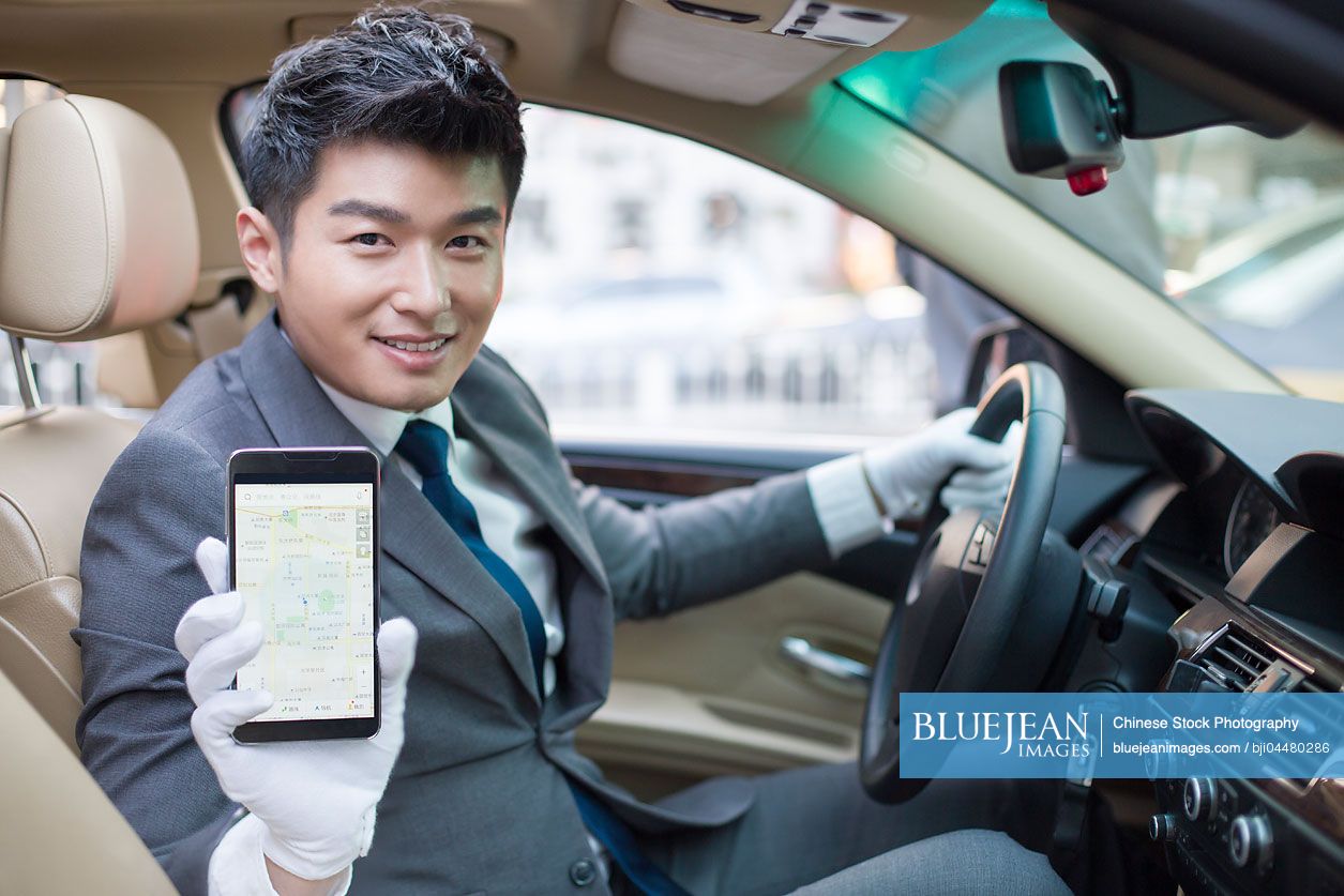 Chinese chauffeur showing smart phone in a car
