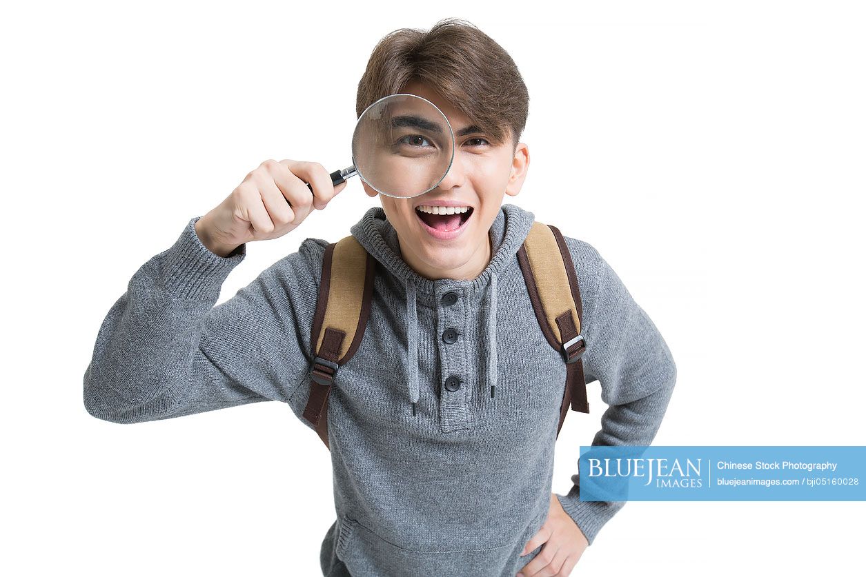 Cheerful male college student looking through magnifying glass
