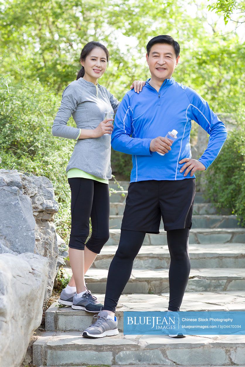 Happy mature Chinese couple holding bottled water after exercising