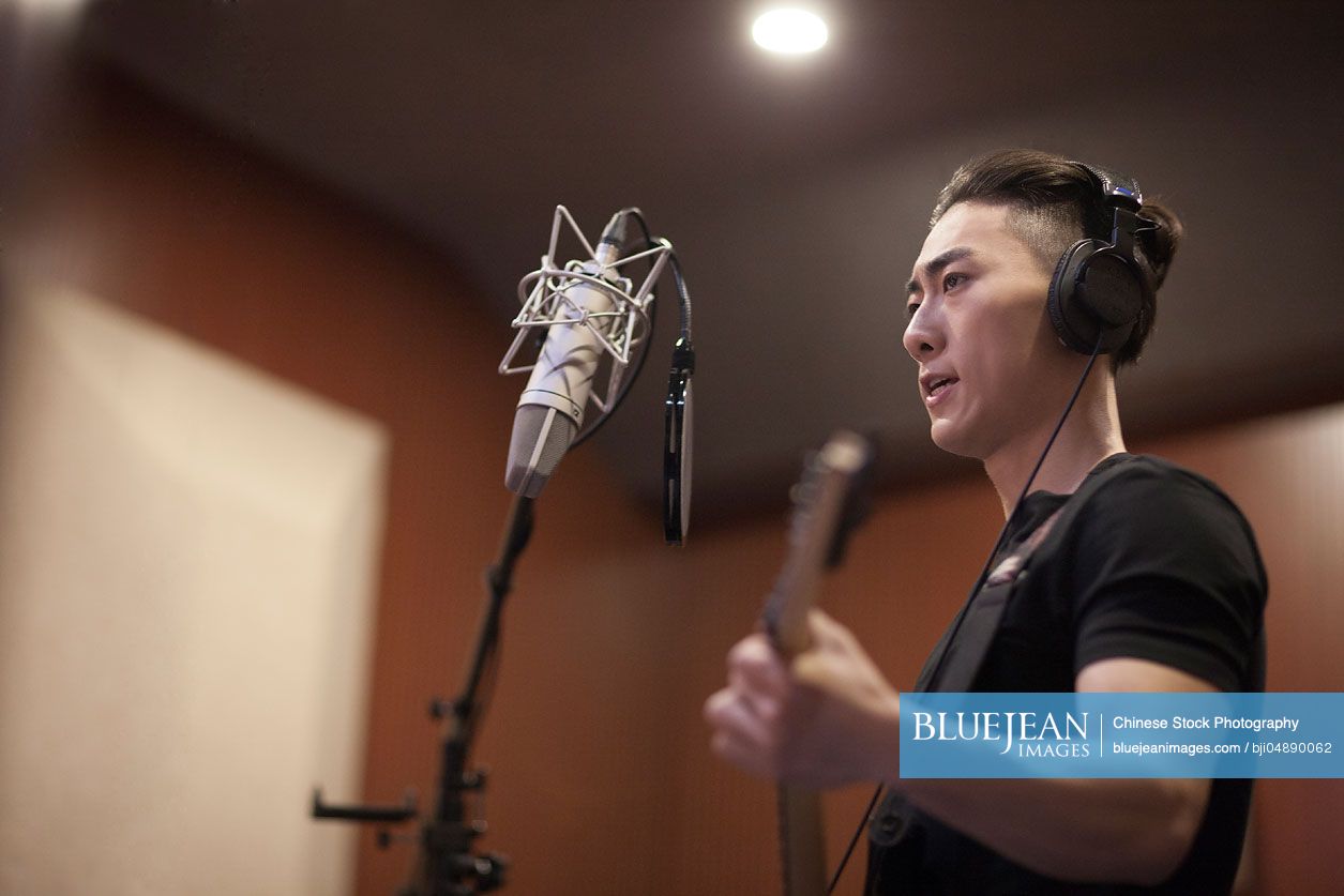 Young Chinese man singing with guitar in recording studio
