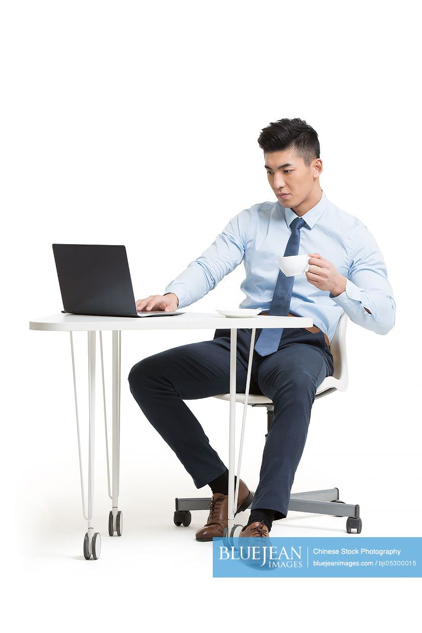 Young Chinese businessman working with laptop in office while drinking coffee