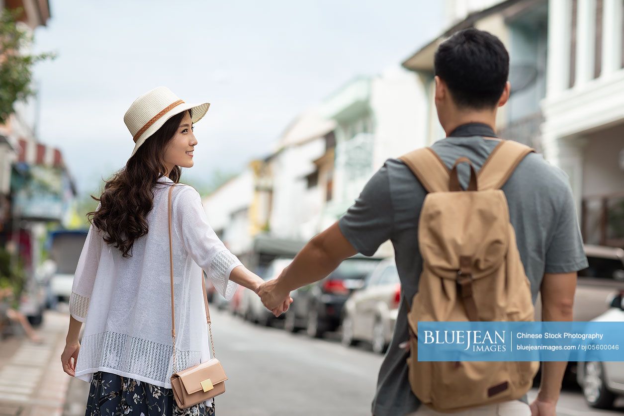 Happy young Chinese couple holding hands on street