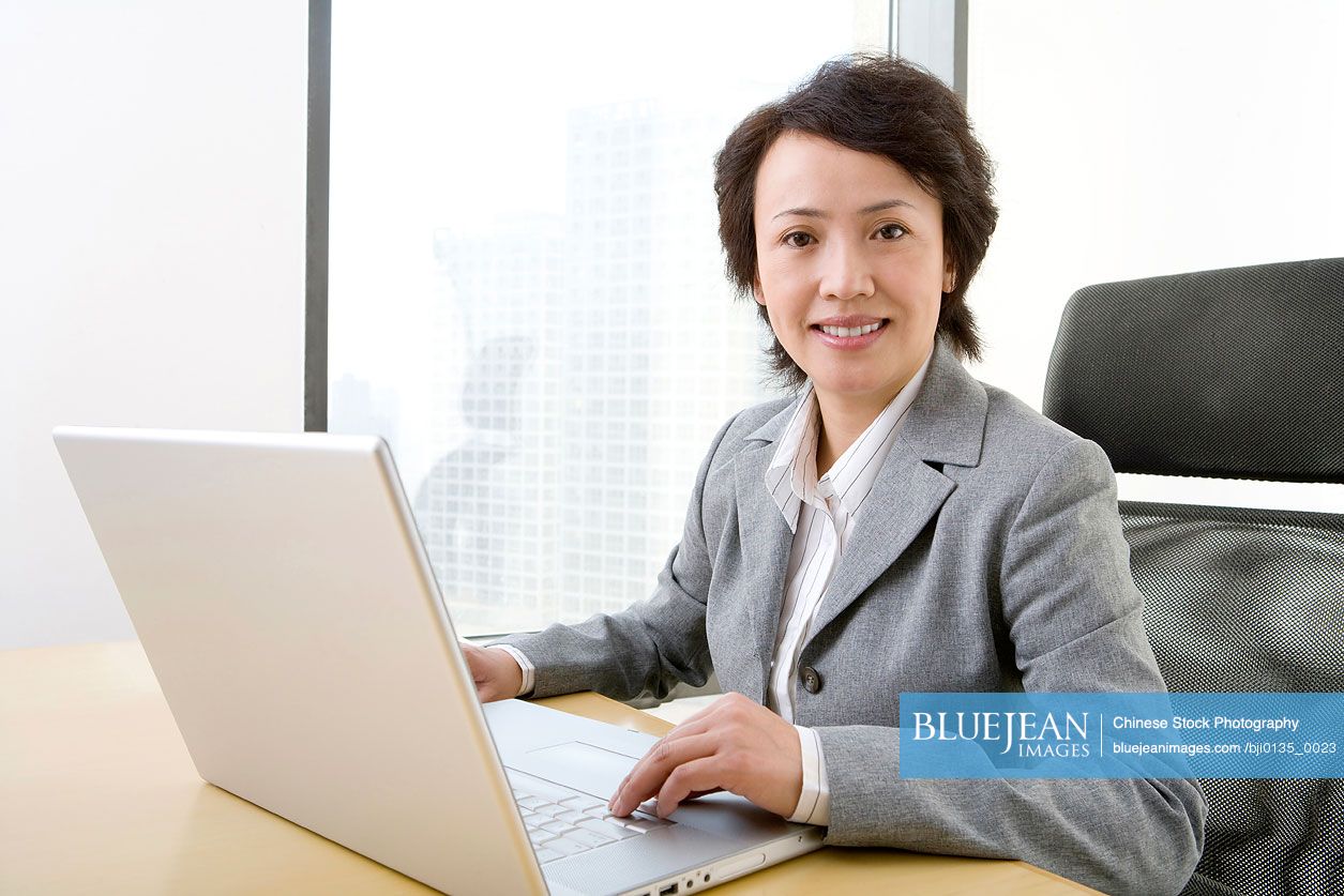 Chinese businesswoman uses laptop in a well-lit, sunny office