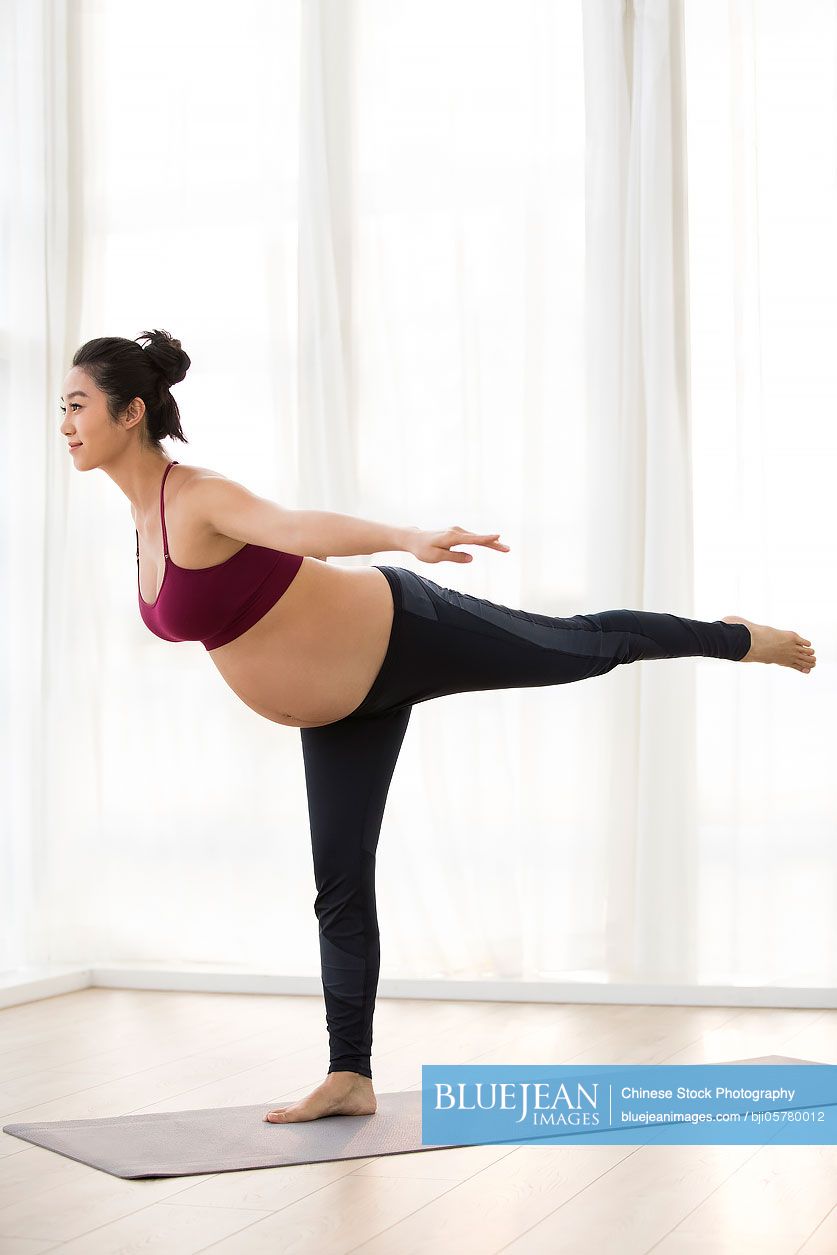 Cheerful Chinese pregnant woman practicing yoga at home