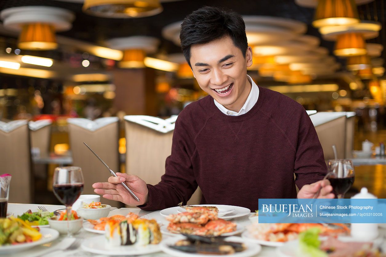 Cheerful young Chinese man having buffet dinner