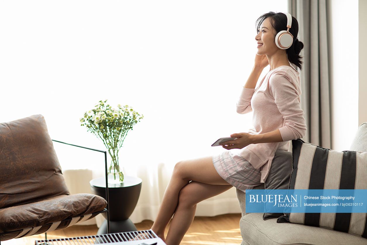 Happy young Chinese woman listening to music in living room