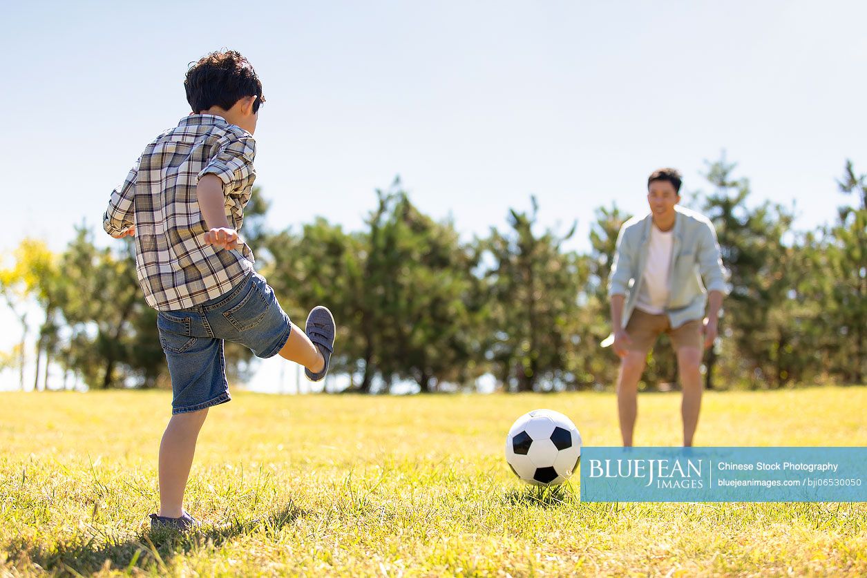 happy-chinese-father-and-son-playing-football-in-park-high-res-stock