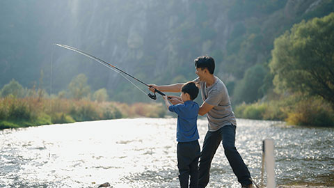 Cheerful Chinese father teaching son fishing