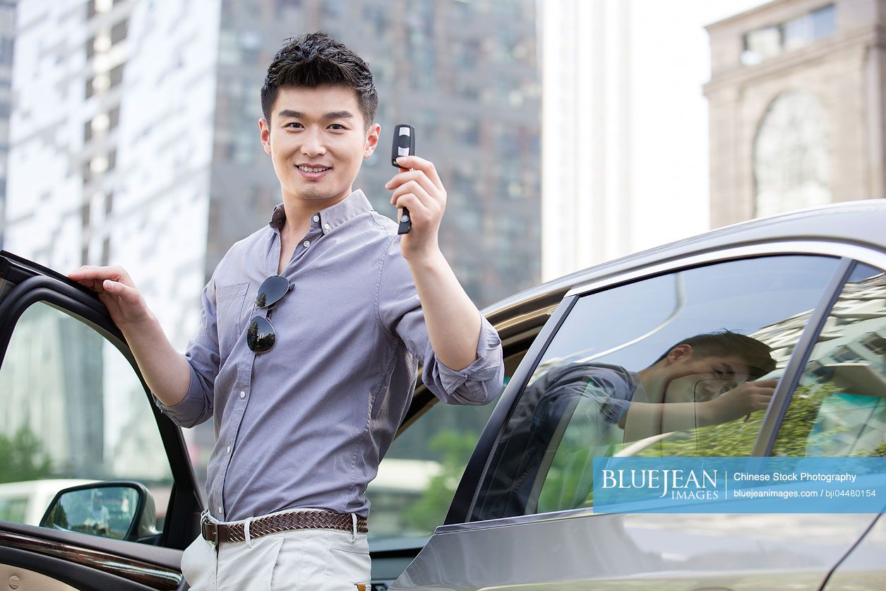 Young Chinese man posing with keys to his new car