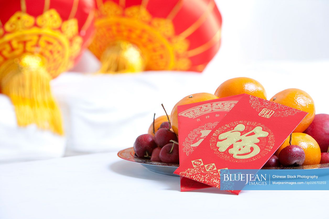 Red envelopes on bowl of fruit and lanterns to celebrate Chinese New Year