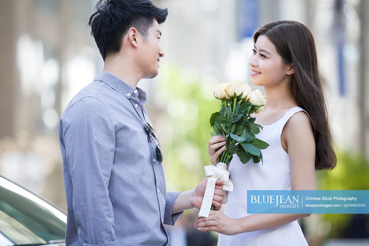 Young Chinese man giving flowers to girlfriend