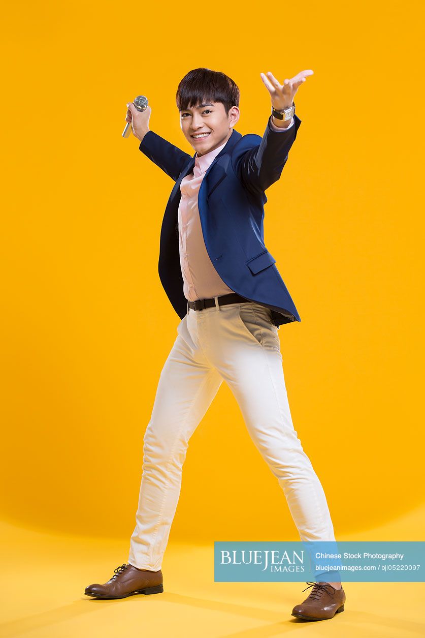 Cheerful young Chinese man singing with microphone