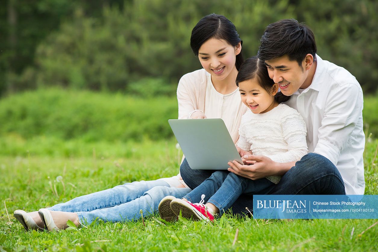 Happy Chinese family using laptop on the grass