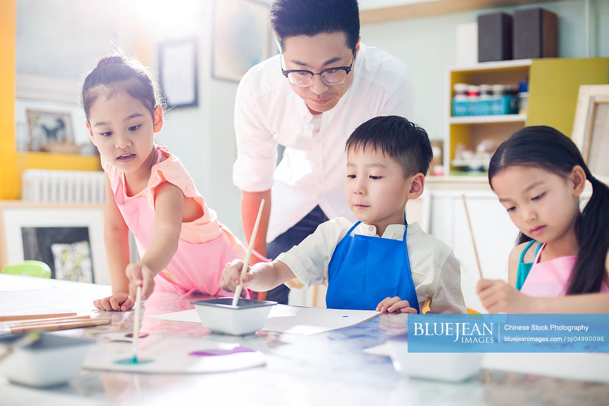 Little Chinese children painting in art class with teacher