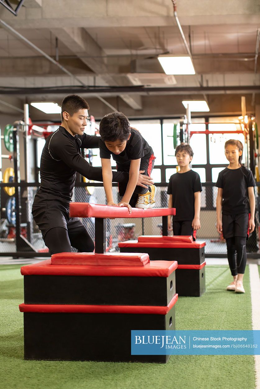 Active Chinese children having exercise class with their coach in gym ...