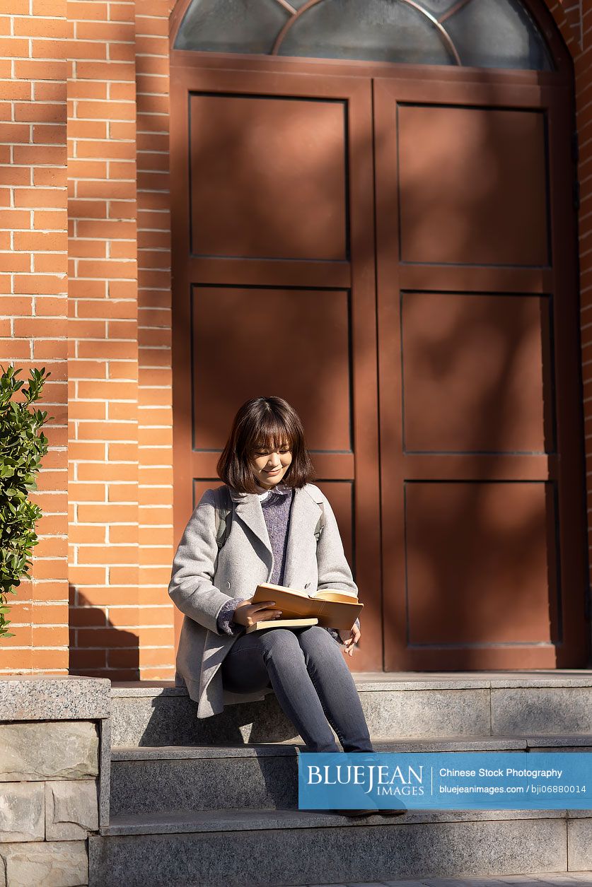 Happy Chinese college student reading on campus